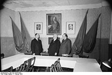 Raum mit Fahnenschmuck und Thälmannbild, davor: Walter Ulbricht, Wilhelm Pieck und Otto Grotewohl.